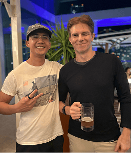 2 people smiling, one giving a peace sign and the other holding a drink