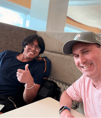 2 people smiling in an office. one is giving a thumbs up