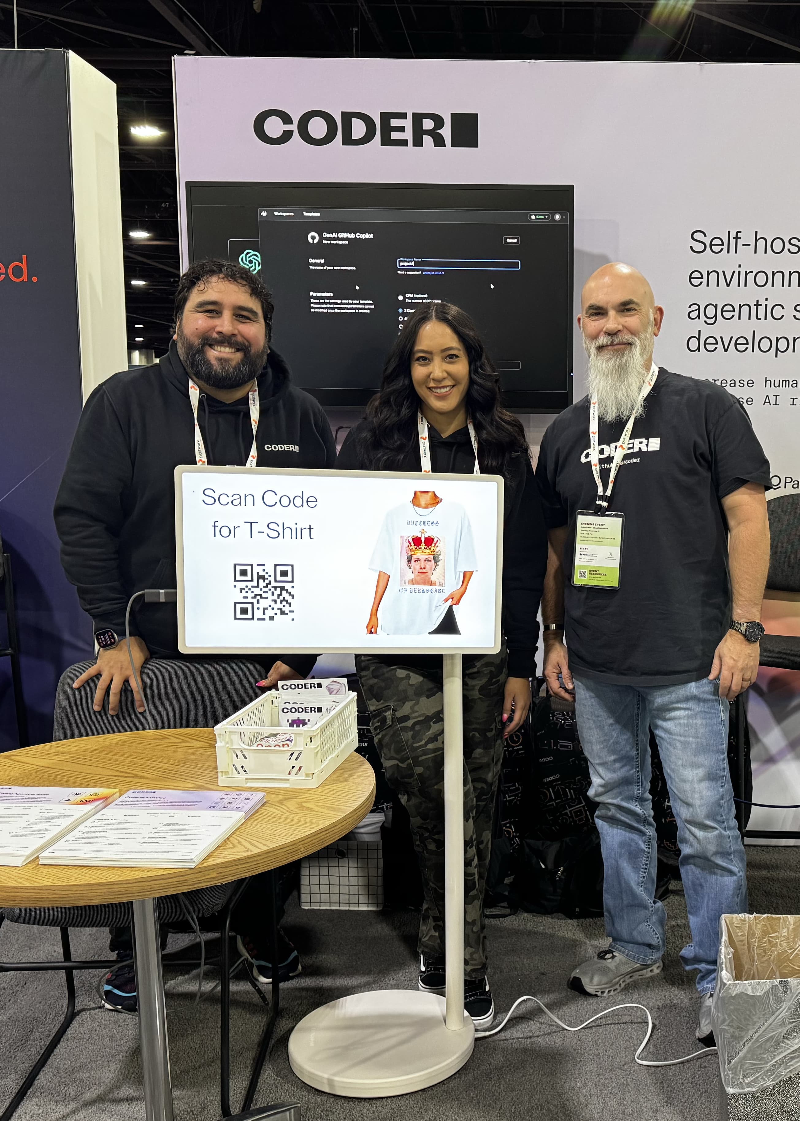 3 people in Coder shirts smiling in front of a backdrop with the Coder logo and a screenshot of a Coder workspace