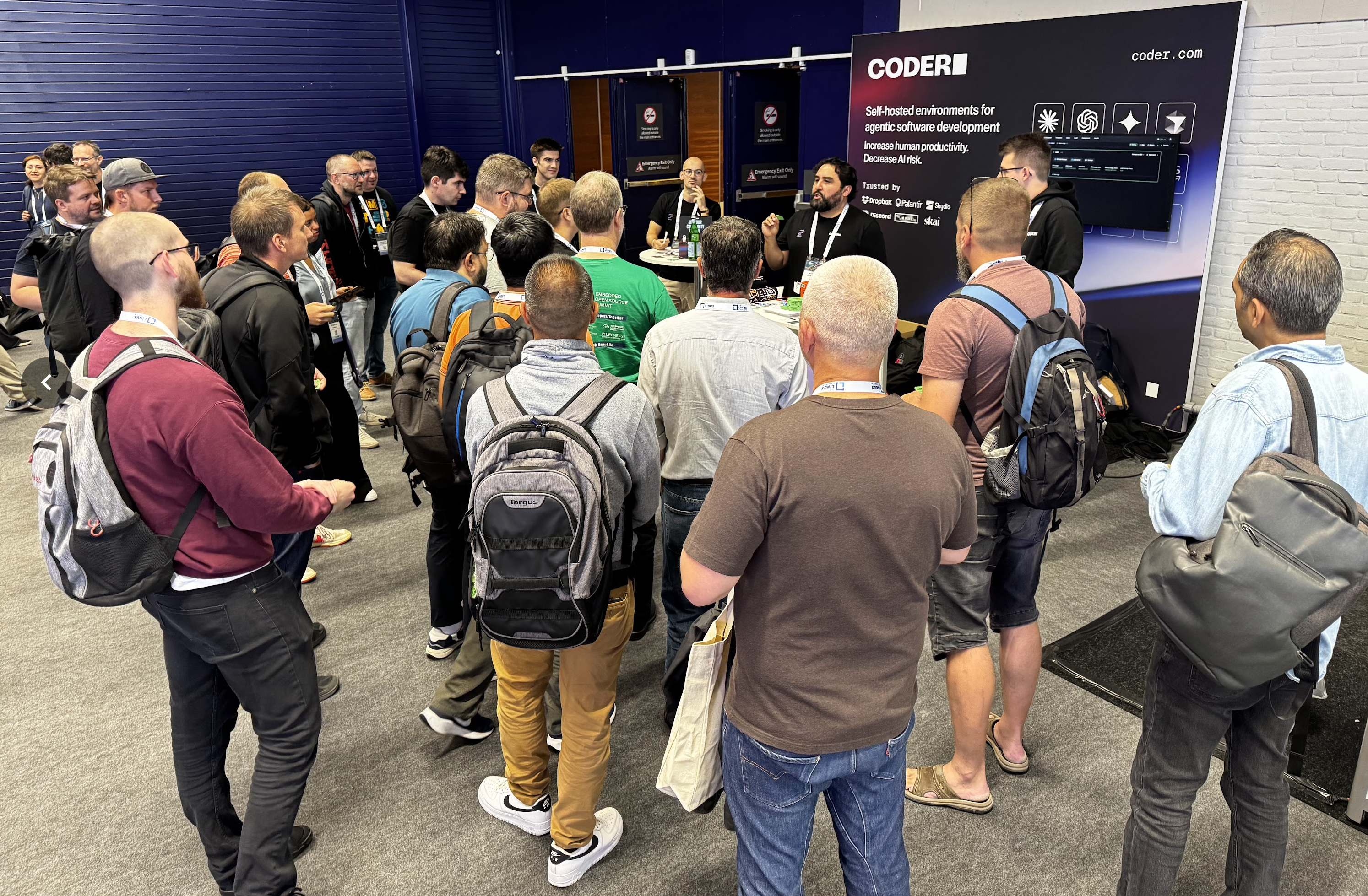 small crowd of people gathered around a Coder conference booth as a person wearing a Coder lanyard addresses them